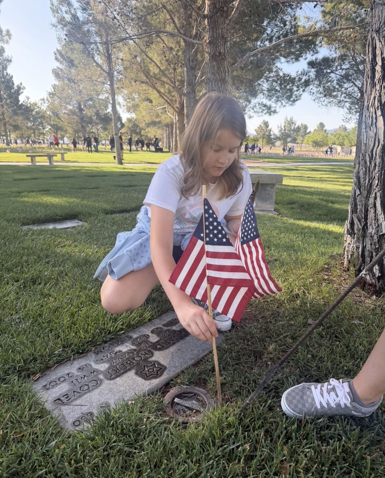 Young girl placing an American flag at a veteran's memorial marker